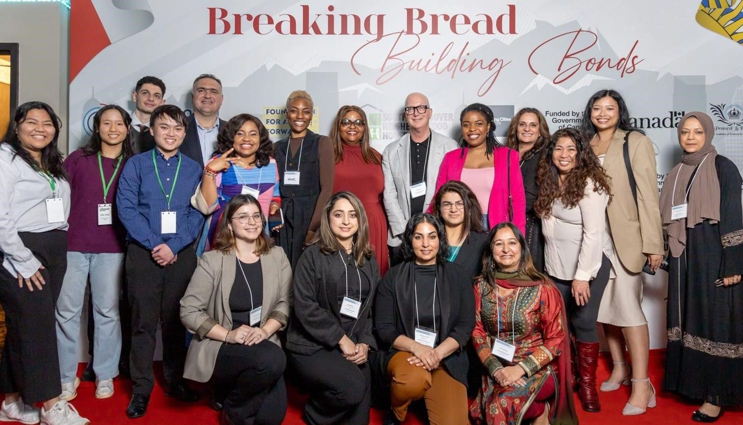 Group of diverse people posing at an event with a backdrop reading 'Breaking Bread Building Bonds.'