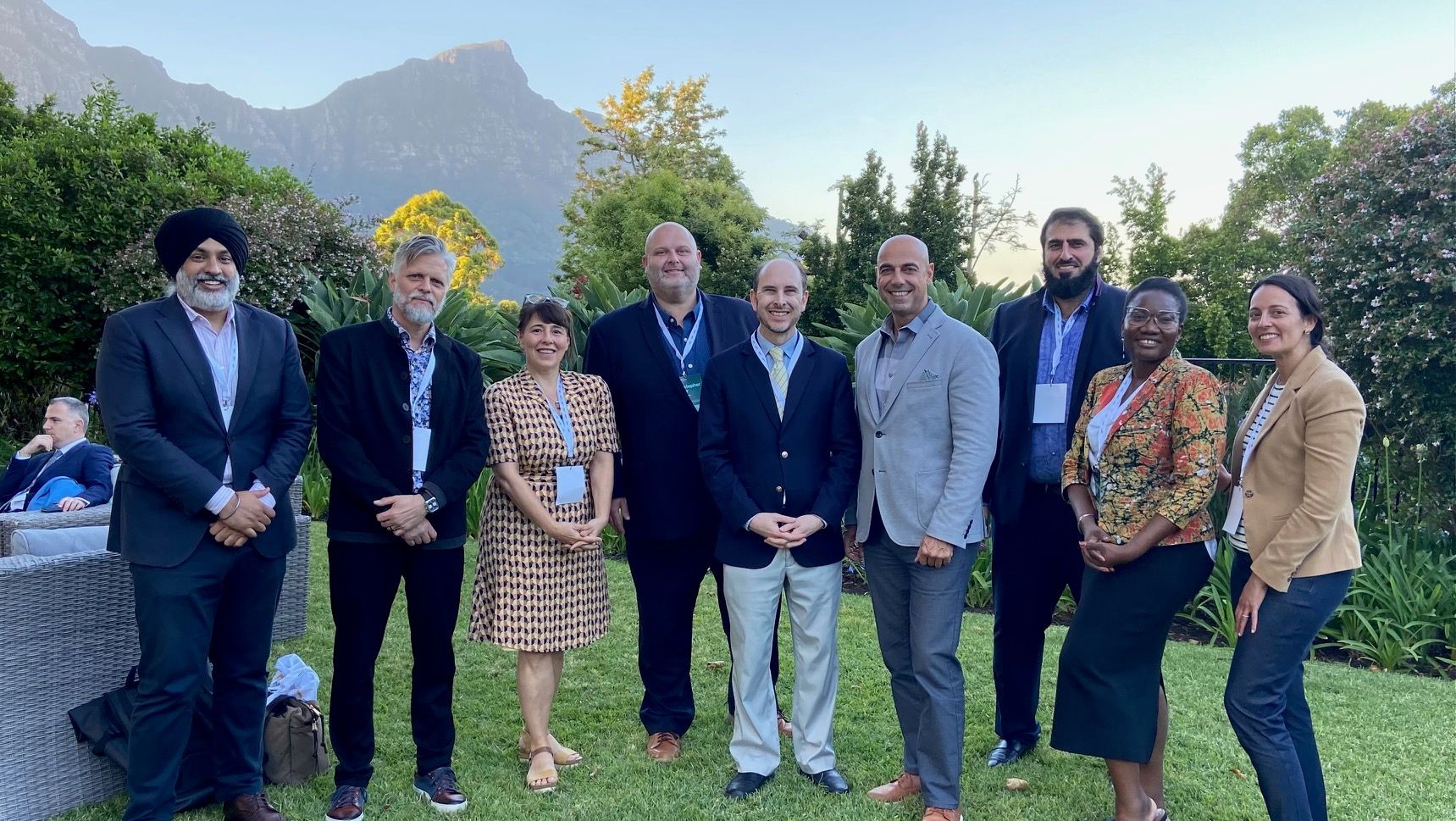 Group of professionally dressed individuals standing together outdoors with a scenic mountain background and greenery.