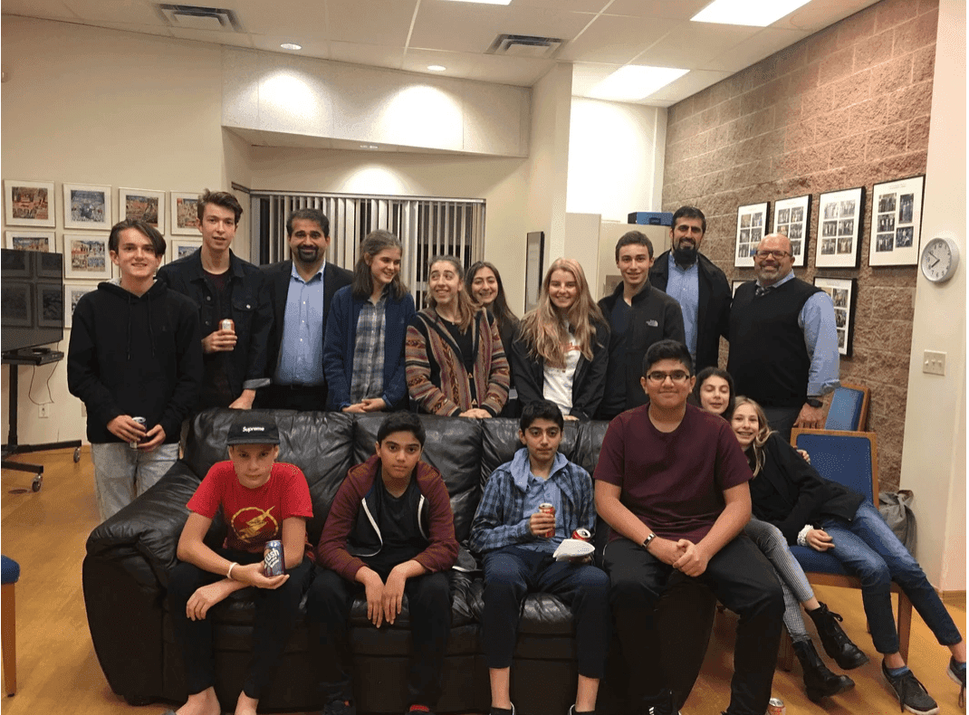 Group of teenagers and adults posing together in a room with framed photos on the walls.