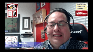 Person wearing glasses and a headset, sitting in an office with framed pictures on the walls.