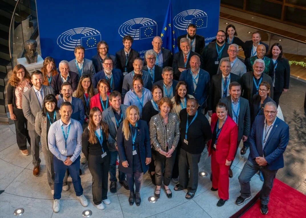 Group of diverse people standing together inside a building with EU flags and logos in the background.