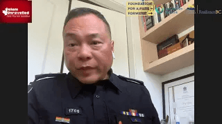 Person in uniform speaking in an office with shelves, certificates, and organizational logos.