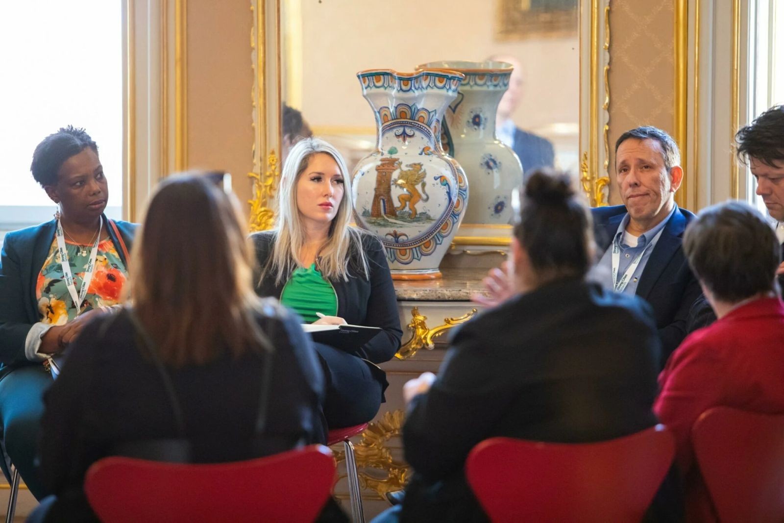 Group of people sitting in a discussion setting, with a decorative vase in the background.