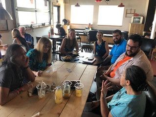 Group of people sitting around a wooden table in a restaurant, engaged in conversation and enjoying drinks.