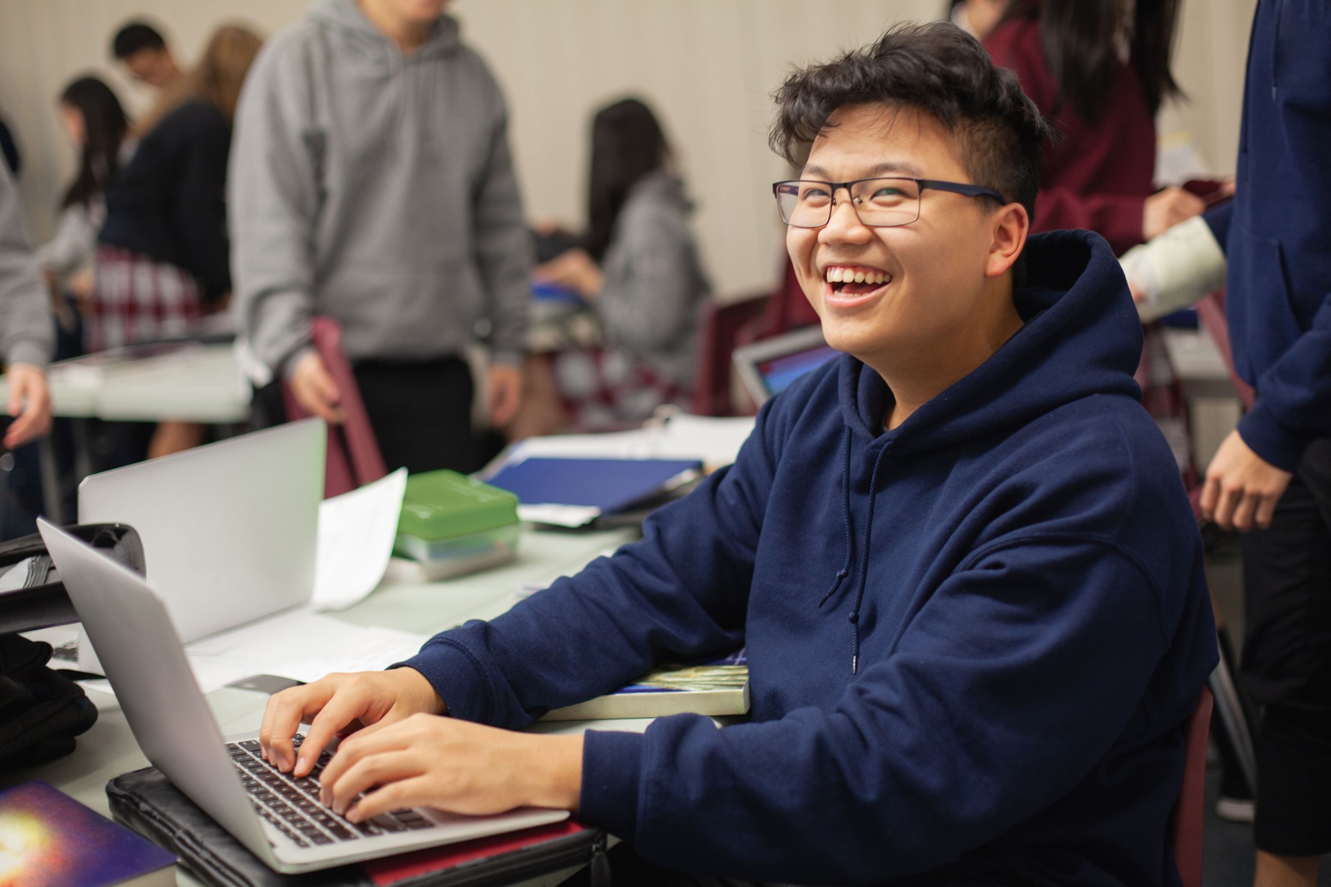 Portrait of Asian Chinese teenage boy in high school classroom smiling typing on laptop computer