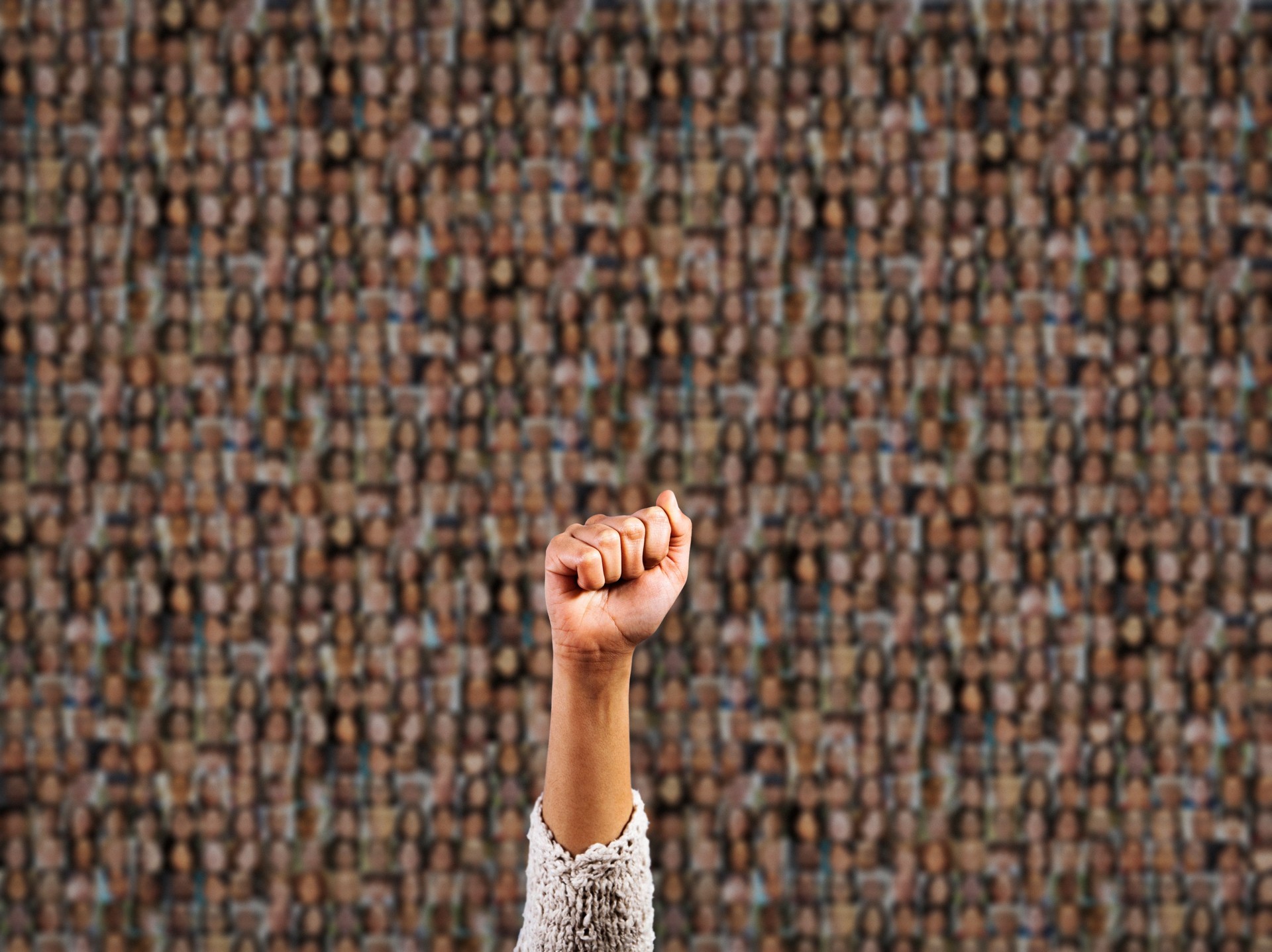 Fighting for humanity: woman's clenched fist rises in front of a group of many people, blurred into abstraction